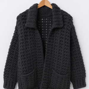 An oversized crochet cardigan in a dark gray color with a textured stitch pattern, a classic collar, and two front pockets, shown hanging on a wooden hanger.