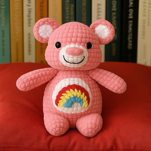 Crochet teddy bear in pink, with a belly patch featuring a rainbow.