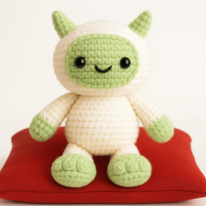 A small, crocheted yeti toy with a cream-colored body and a light green face, hands, and feet, representing a Free Yuti the Yeti Amigurumi Crochet Pattern.