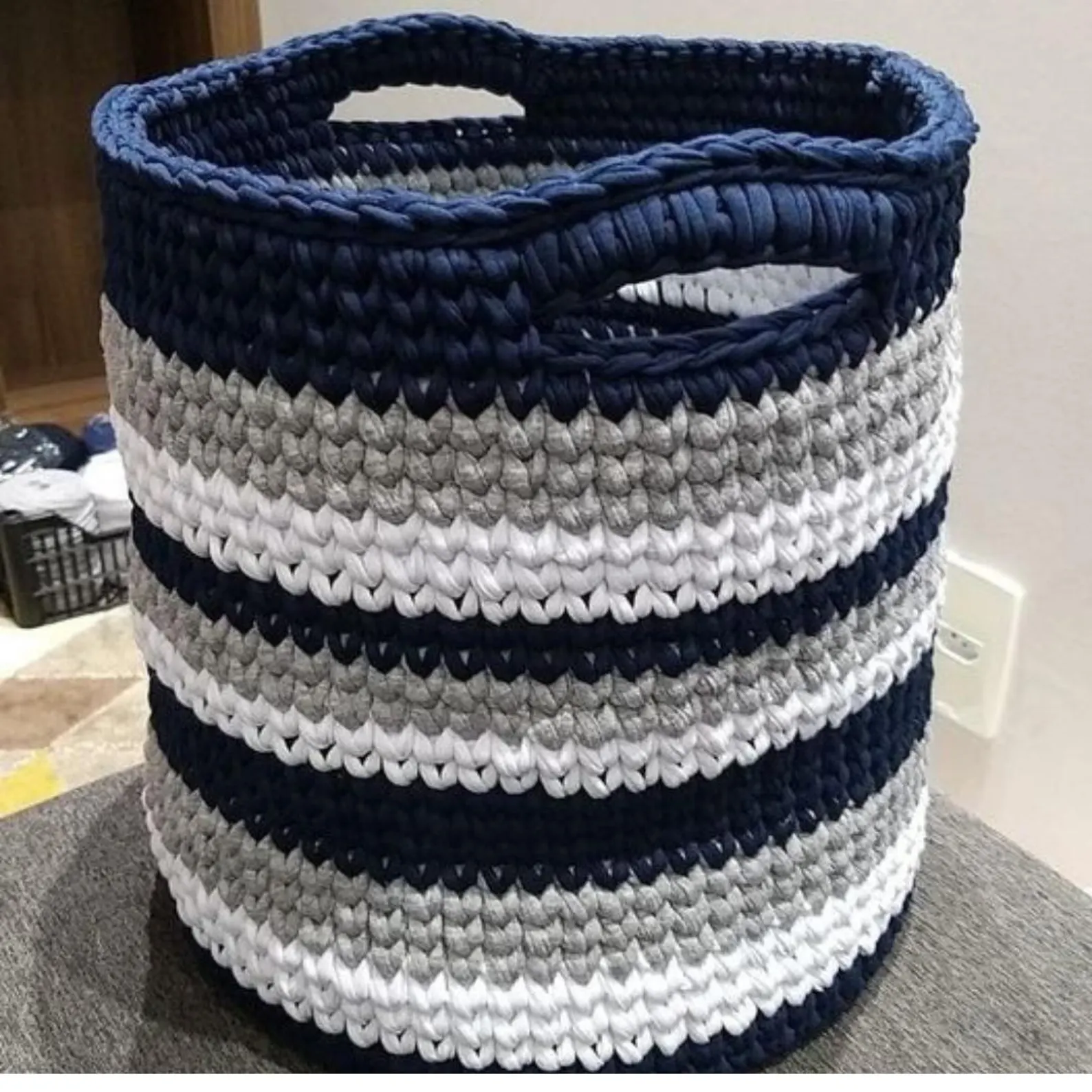 Large round crocheted t-shirt yarn storage basket with built-in handles, featuring alternating stripes of navy blue, light grey, and white.
