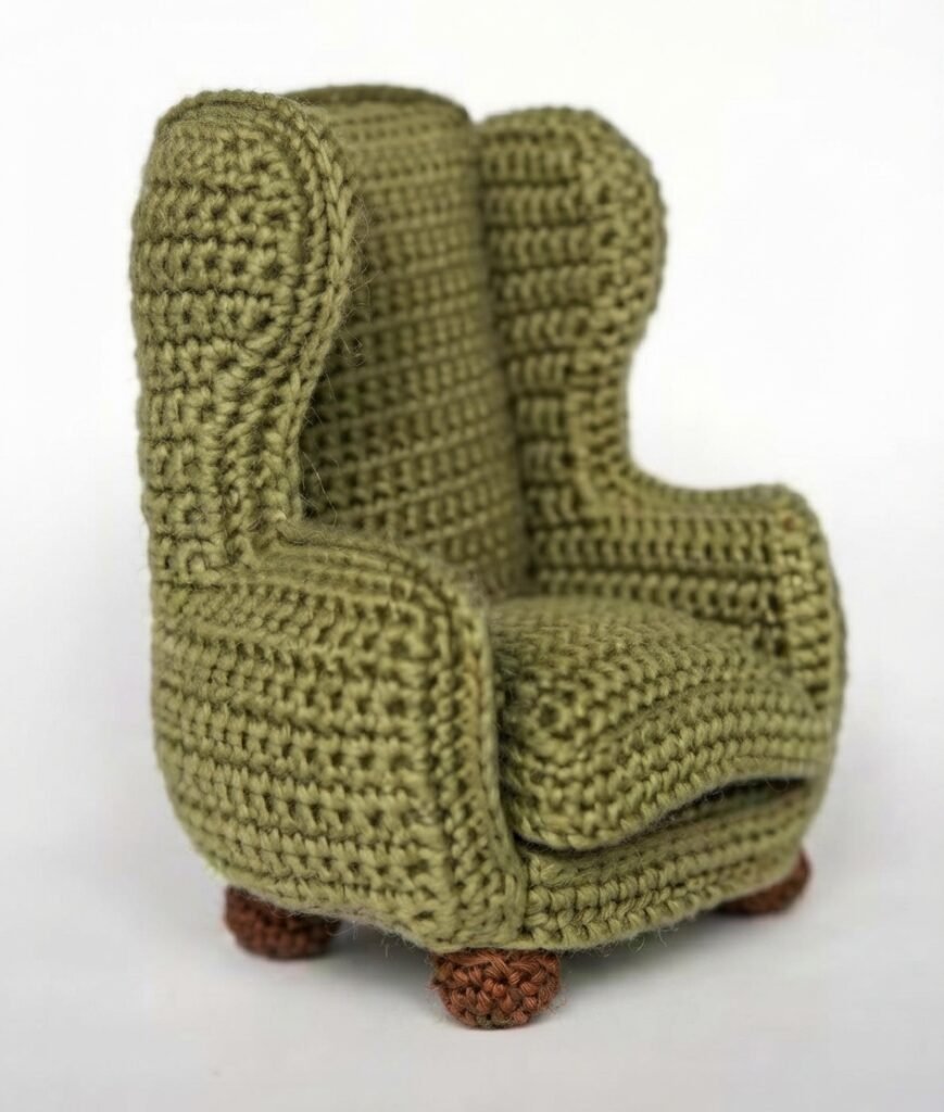 High-resolution photo of a miniature moss-green crocheted wingback armchair with textured brown wooden-style feet, displayed against a plain white background.