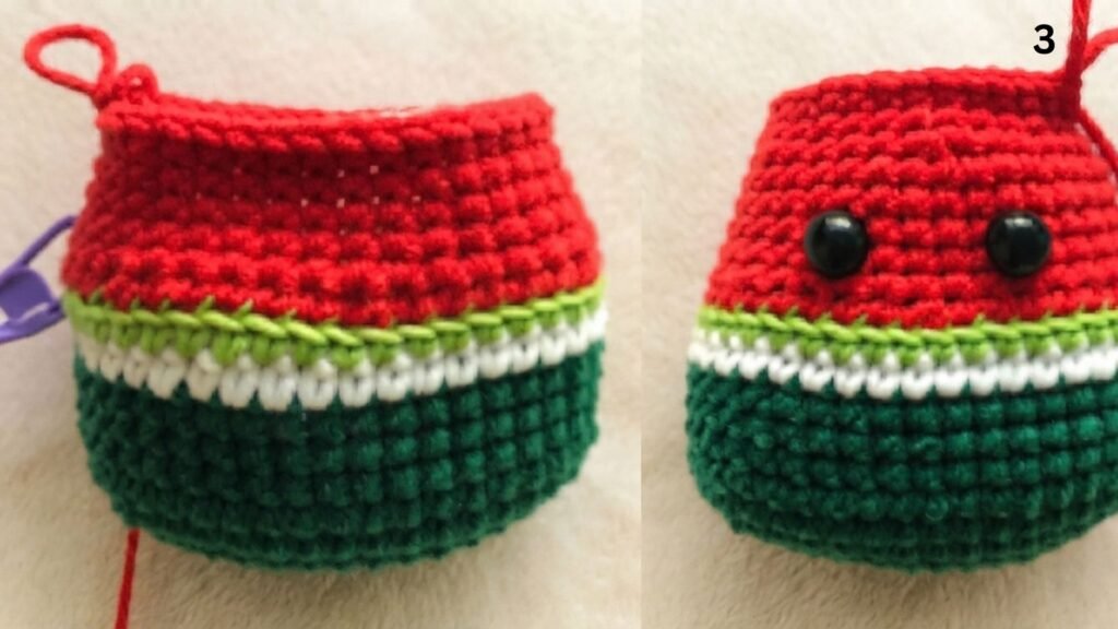 Step 3 of a free watermelon keychain crochet pattern, showing two views of the crocheted piece with dark green, white, light green, and red sections, safety eyes attached to the front, and the number '3' in the corner, all on a light beige background.